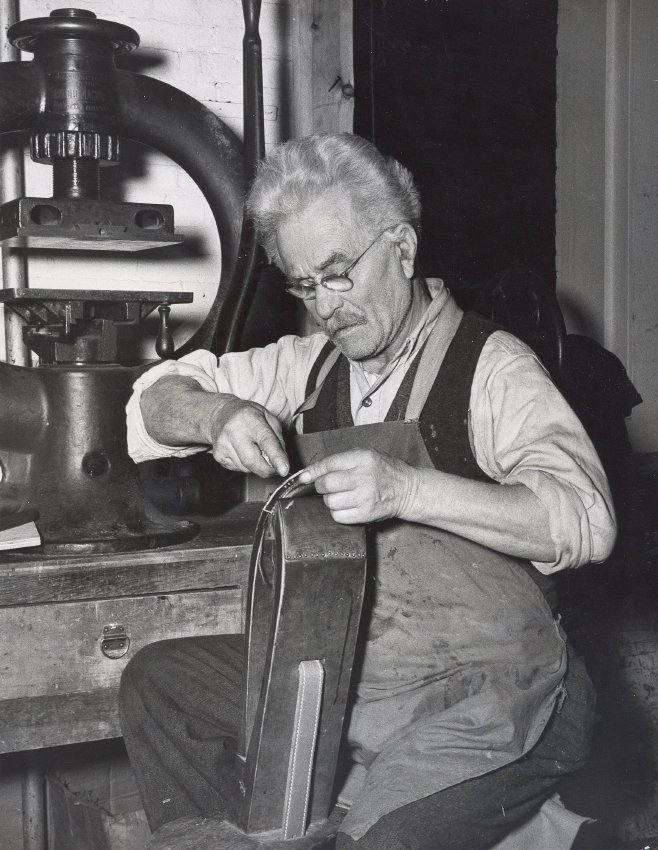Frederick J. Gerstmeyer seated at a saddler’s clamp, working on leather in the Oshkosh Trunk Company’s leather department, 1947.