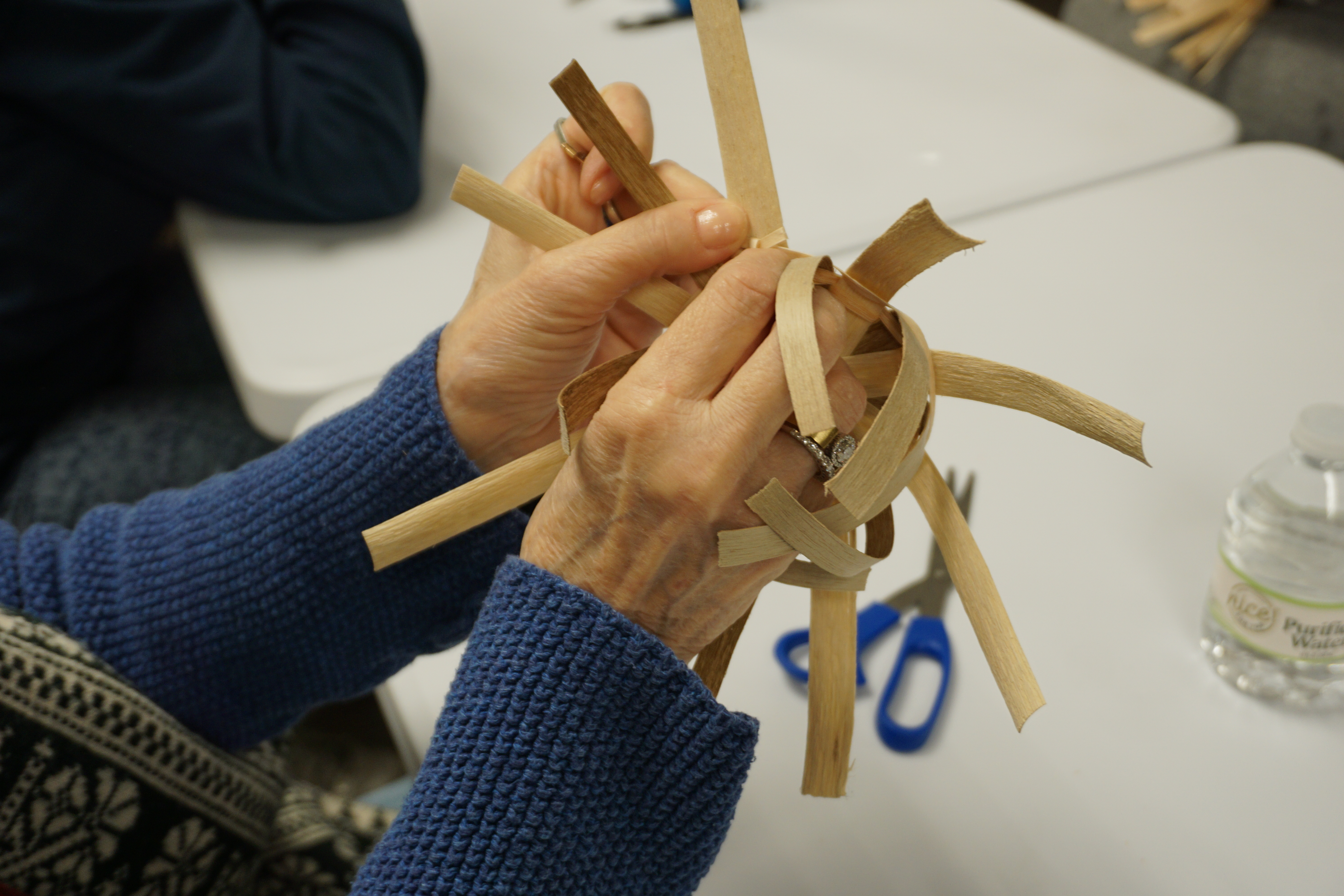 Image of a person's hands weaving black ash into a basket